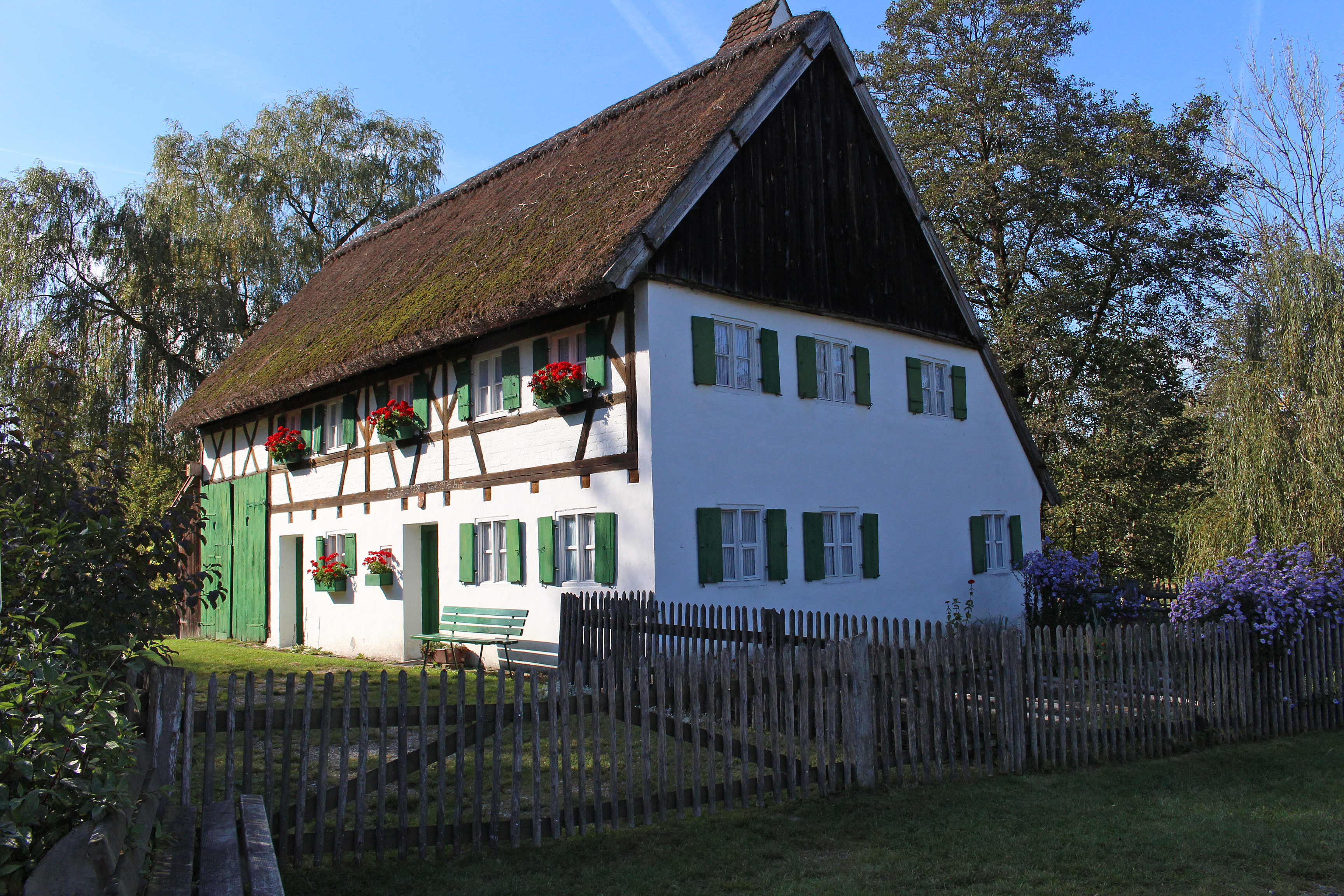 Staudenhaus mit Strohdach, grünen Fensterläden, Blumenkästen