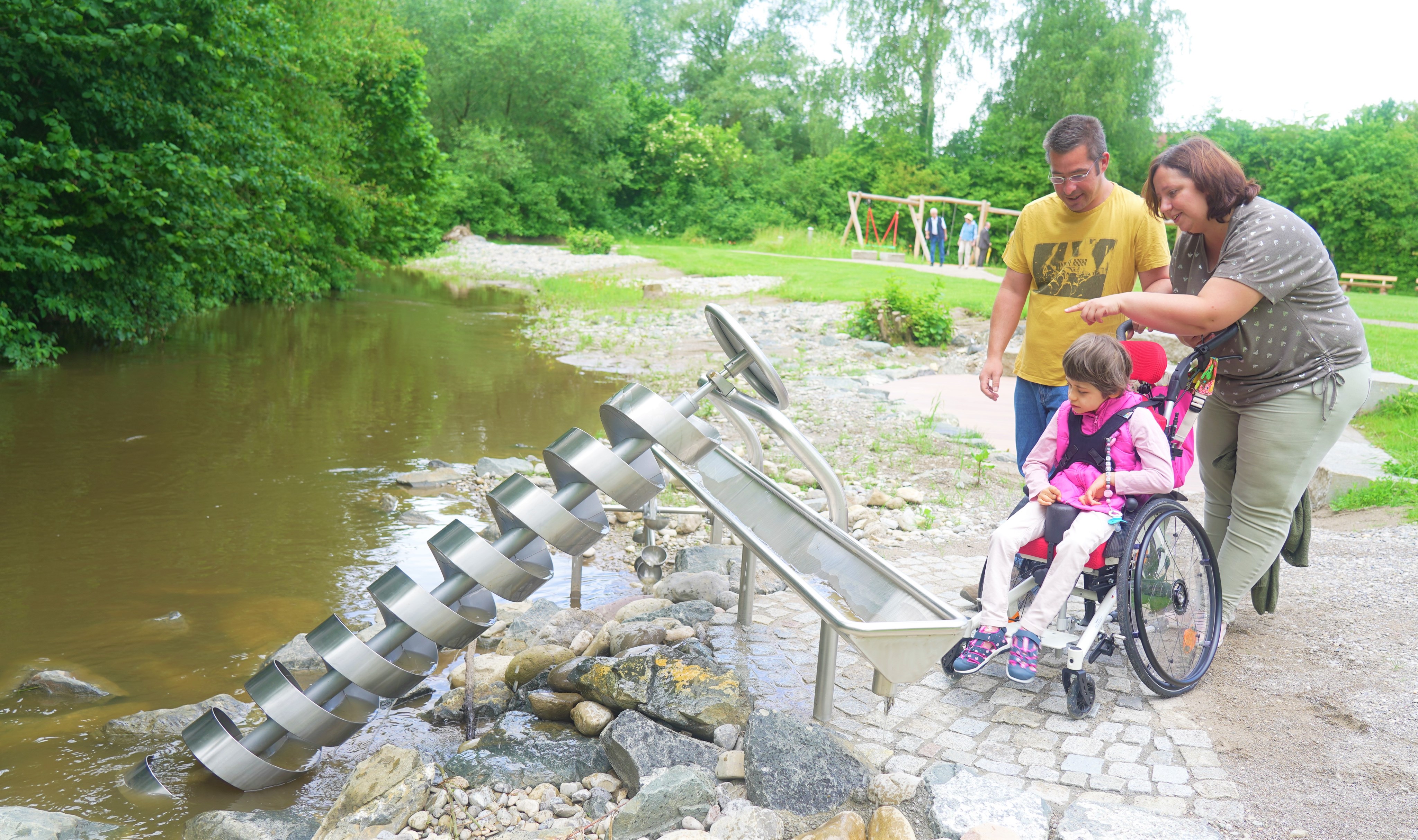 Vater, Mutter und Kind mit Rollstuhl am Bachlauf